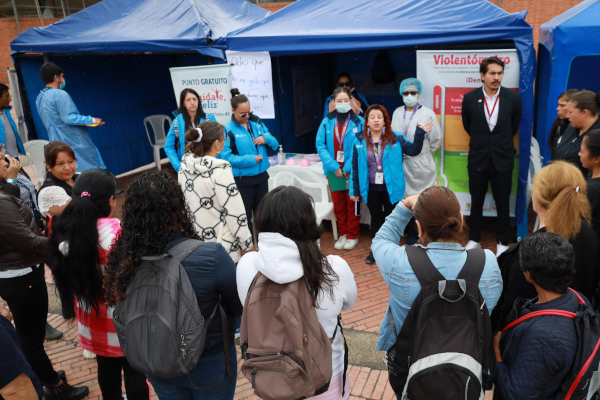 Mujeres reunidas escuchando a otras. De fondo se ven unas carpas de color azul claro.