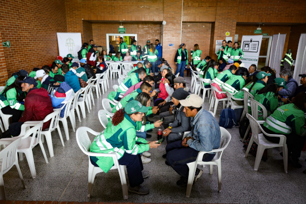 Foto al interior de un auditorio. Se ven seis filas de sillas ocupadas por recicladores de oficio quienes están siendo atendidos por profesionales de la UAESP que portan chaqueta verde