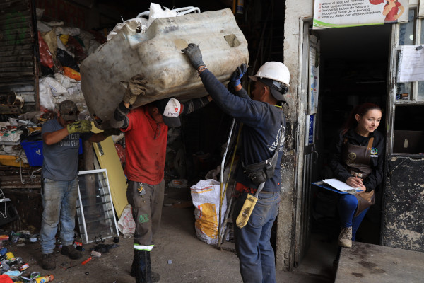 Personas dentro de una bodega de reciclaje, manipulando residuos. Varios hombres alzan bolsas con residuos.