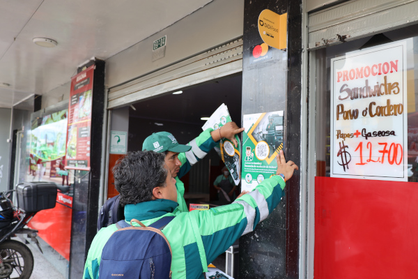 Funcionarios de la UAESP ponen afiches con la información de la recolección de residuos en la zona sensibilizada.