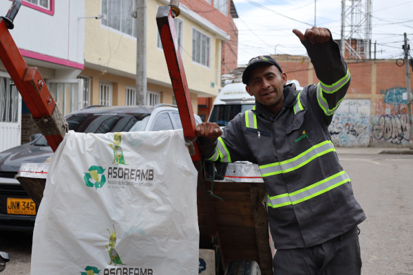  Foto en el interior de una bodega. En ella se ve a un reciclador con el dedo arriba, en actitud positiva. El reciclador porta el uniforme