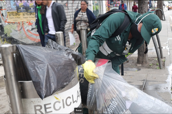 Operaria de aseo vacía cesta de residuos en vía pública.