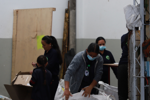 Foto de noche. Mujeres en una bodega de reciclaje haciendo sepración de residuos. Algunas tienen uniforme color azul oscuro.