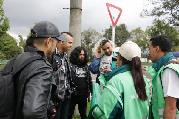 Foto en exteriores y de día. Foto en el Parque Simón Bolívar, plano medio. 3 hombres (jóvenes) están recibiendo información de los gestores sociales de la UAESP sobre separación en la fuente.