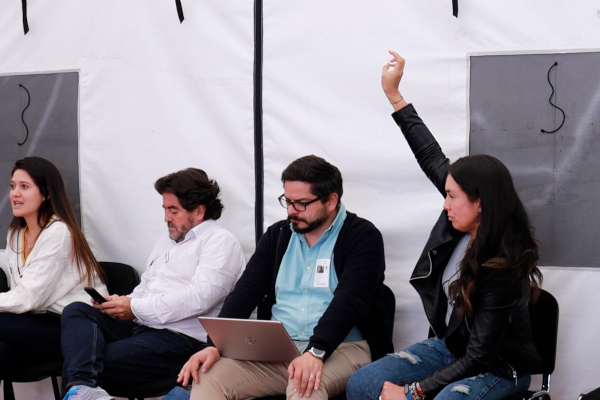 Cuatro personas sentadas participando de la Mesa de Plástico. Una de ellas, de chaqueta negra está levantando la mano pidiendo la palabra. Las otras; una está mirando el computador, otra su celular y otra está interviniendo. 