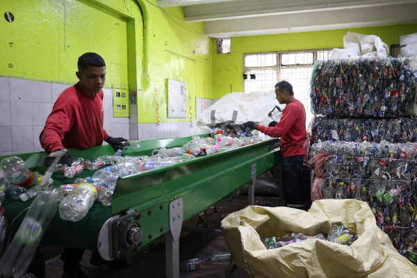 Dos recicladores están separando material plástico en una banda transportadora.