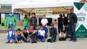 Niños y niña con funcionarios de la UAESP mirando a la Cámara. En el stand de disposición final en actividad de rendición de cuentas.