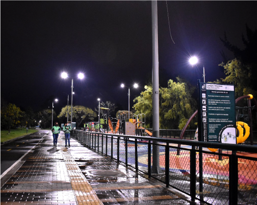 En la imagen: Una foto nocturna iluminado con luz blanca, se ve un parque y su zona de juegos