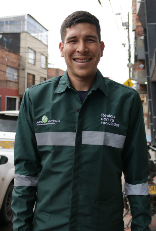 En la imagen: En primer plano, un reciclador de uniforme verde oscuro muestra una gran sonrisa. De fondo unas casas.