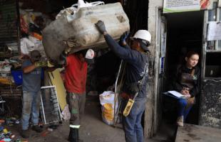 Personas dentro de una bodega de reciclaje, manipulando residuos. Varios hombres alzan bolsas con residuos.