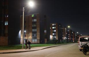 Un hombre y una mujer observan al fondo la Carrera 91 con la nueva iluminación. La pareja se encuentra junto a una bicicleta. 