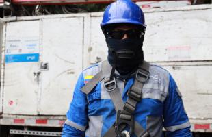 Imagen de uno de los operarios de alumbrado público con el uniforme de Enel Colombia. Los técnicos por trabajar en altura, tienen casco, jafas de protección, arnés y overol. Si evidencias a personas sin estos elementos manipulando elementos de alumbrado denuncia en las Línea 123, 115 y 601 5 115 115.