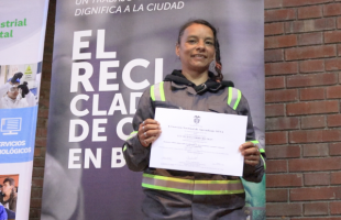 Una mujer con overol de recicladora sostiene en sus manos un diploma.  