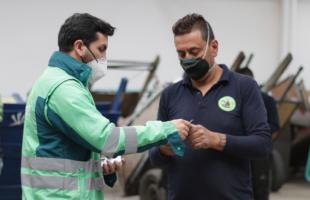 Foto en interior de un CTCC, en ella aparece un profesional de la UAESP con su chaqueta de dos ganas de verde, un reciclador/carretero que viste una camisa azul oscura está a su lado, recibiendo un carnet. En el fondo se ven carretas con material y un carretero se ve a espaldas.