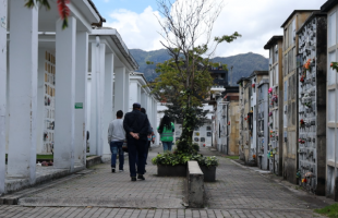 Imagen de una familia caminando al lado de una de las psicólogas de la UAESP, frente a uno de los mausoleos en el Cementerio Distrital del Norte.