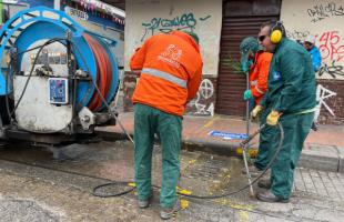 Tres técnicos limpiando alcantarillas y al lado izquierdo está el vehículo Vactor.