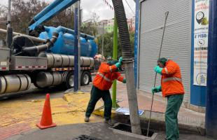 Dos técnicos limpian un sumidero afectado por residuos, al fondo de ve un vehículo, Vactor.