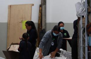 Foto de noche. Mujeres en una bodega de reciclaje haciendo sepración de residuos. Algunas tienen uniforme color azul oscuro.