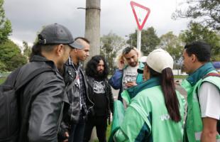 Foto en exteriores y de día. Foto en el Parque Simón Bolívar, plano medio. 3 hombres (jóvenes) están recibiendo información de los gestores sociales de la UAESP sobre separación en la fuente.