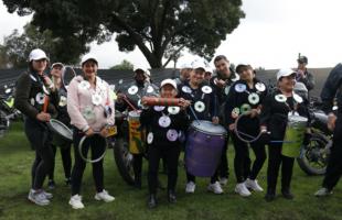 Foto de día, en exteriores en el Parque Simón Bolívar, Plano general.  En la foto se ve un árbol de fondo. Sobre el prado se encuentran 12 personas que se dedican al reciclaje en la ciudad, están acompañados de instrumentos reciclados y artesanales.