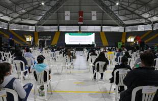 Varios recicladores sentados en un coliseo, escuchando a funcionarios de la UAESP.