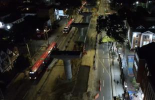 Vista aérea nocturna del corredor de la avenida Caracas, donde se observan las obras del tramo 5 de la Línea 1 del Metro de Bogotá y la operación de TransMilenio.