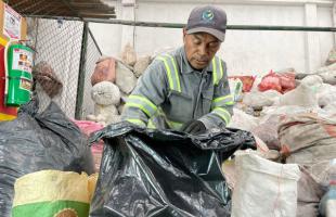 Un reciclador seleccionando materiales y en el fondo se ven bolsas con material reciclable